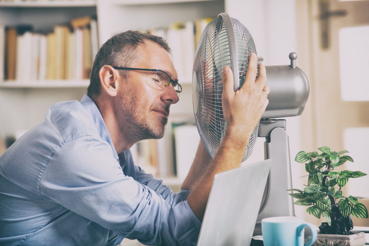 L'homme souffre de chaleur alors qu'il travaille au bureau et essaie de se rafraîchir par le ventilateur